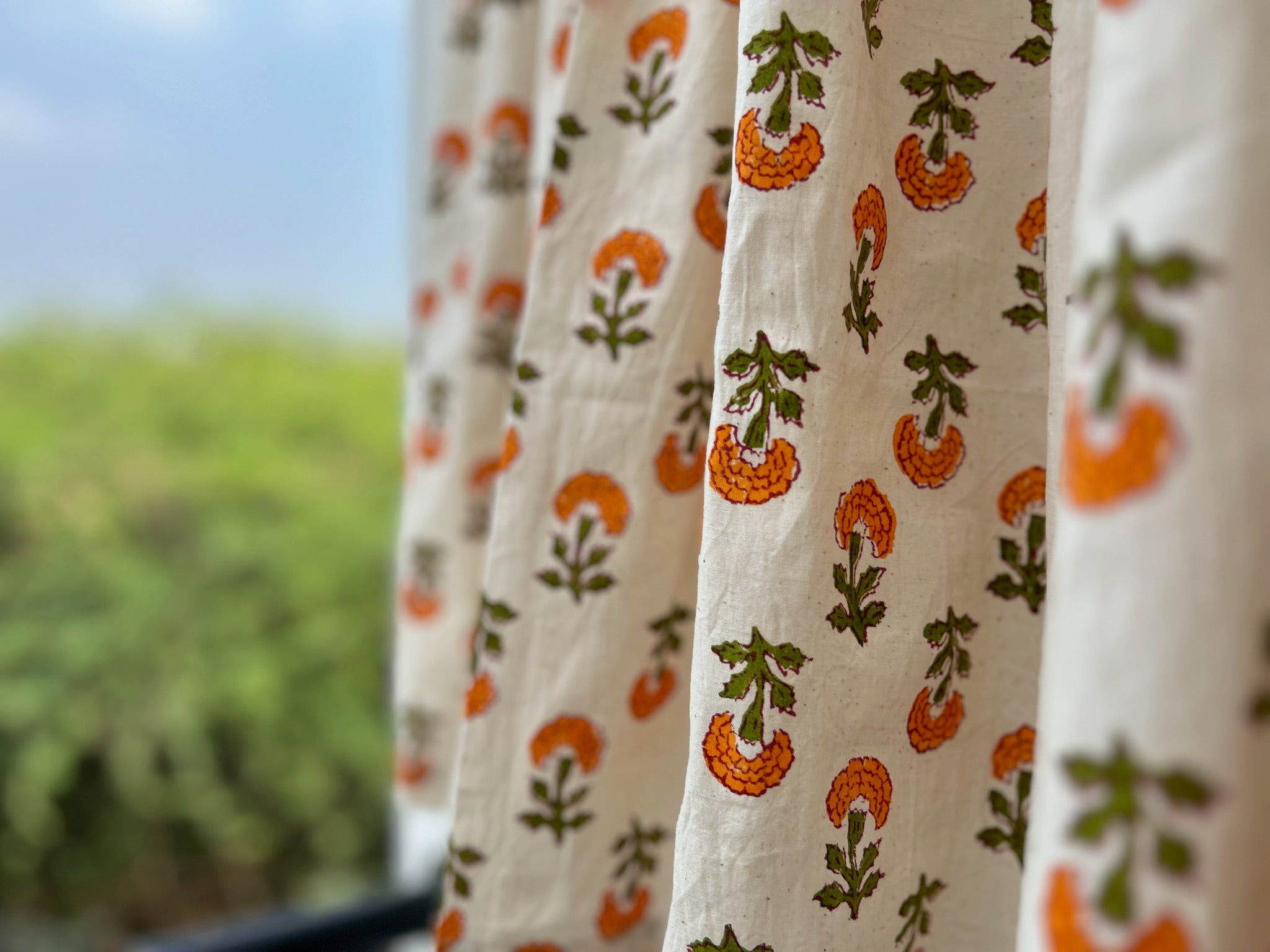 Curtains with orange and green pattern in front of a blurred outdoor background