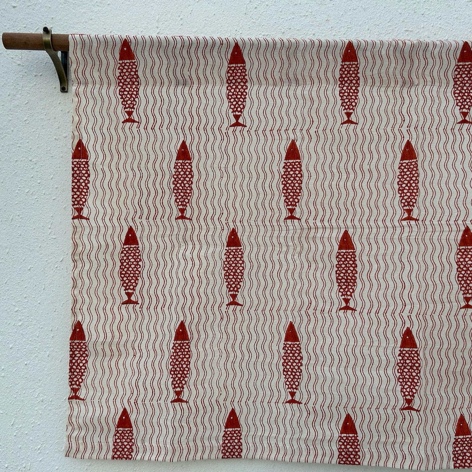Textile with red fish pattern on a beige background, hanging against a white wall.