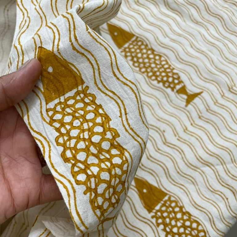 Hand holding fabric with gold fish pattern on a white background