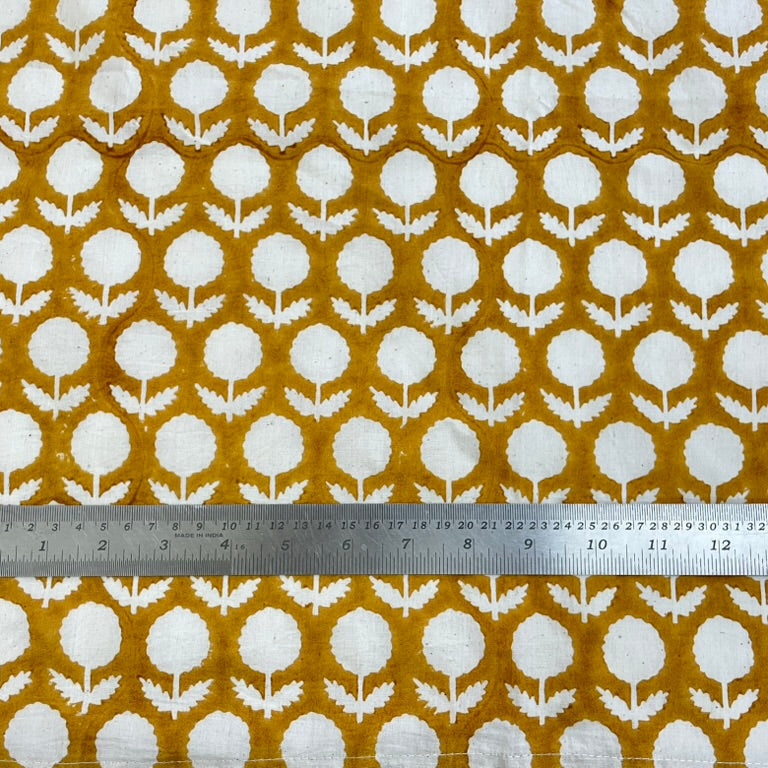 Fabric with white floral pattern on a mustard yellow background, measured by a ruler.