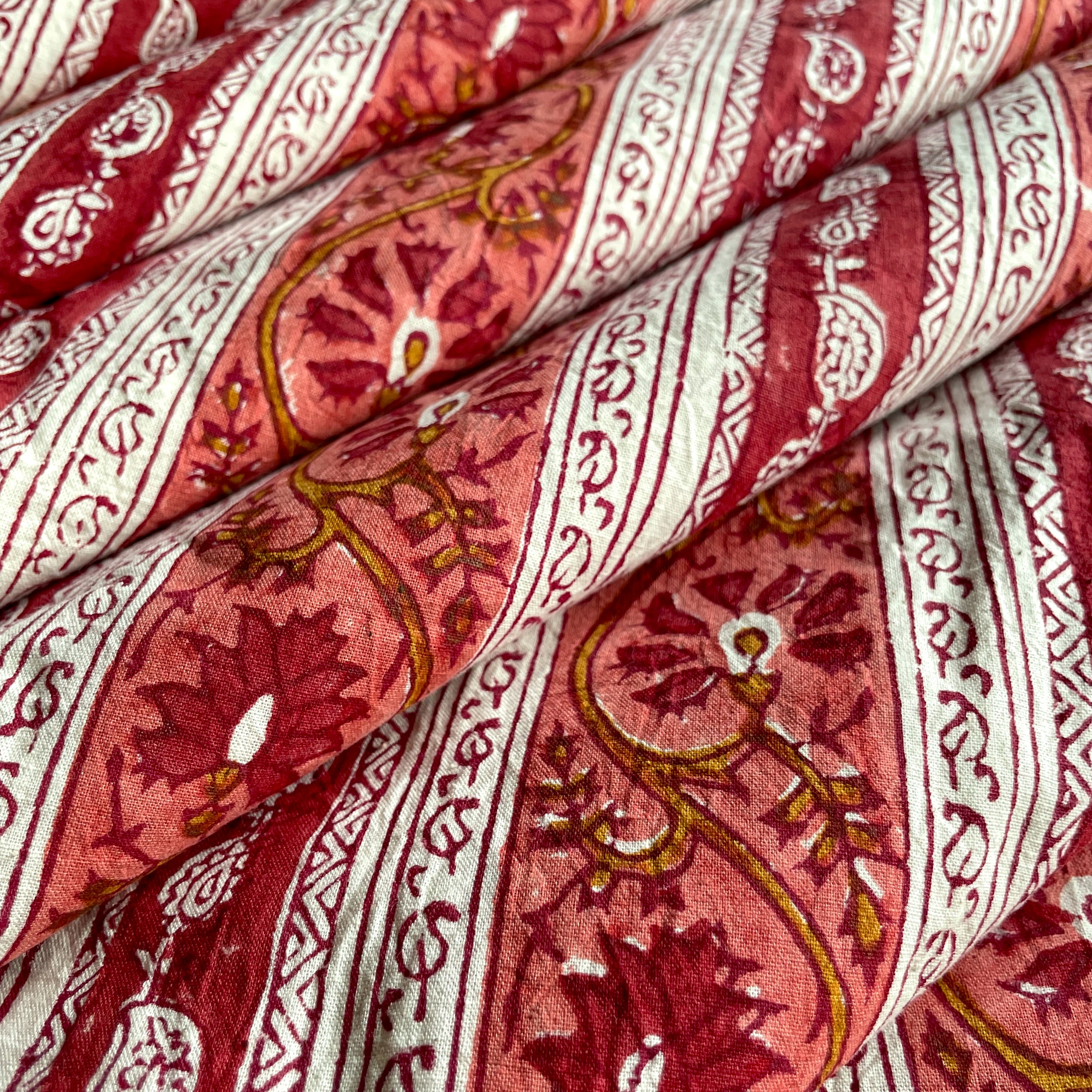 A close-up of draped patterned fabric with a rust and mustard floral design, cream vertical stripes, and vine motifs