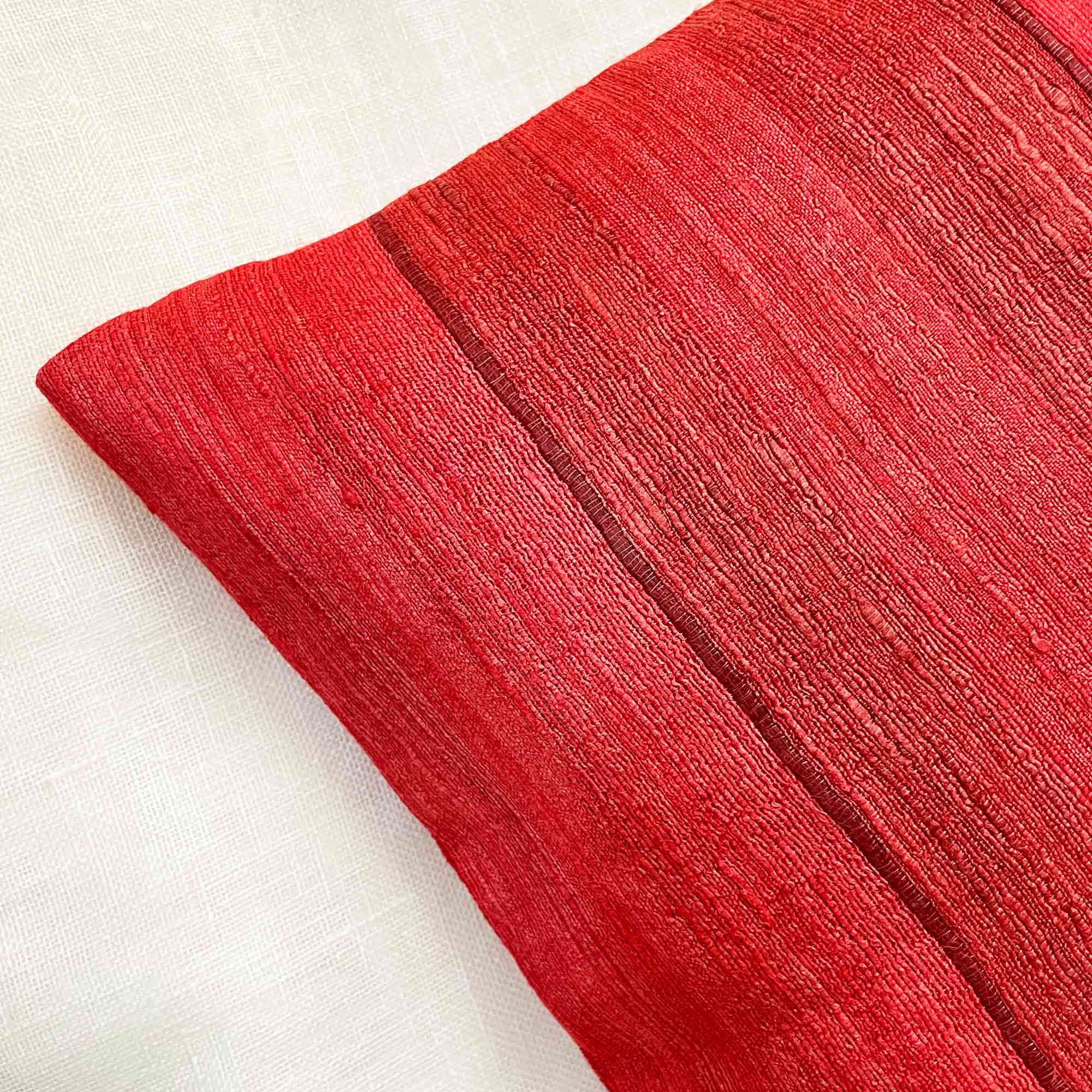 Styled red striped tussar silk pillow cover emphasizing handcrafted weave, subtle sheen, and heritage fabric appeal.