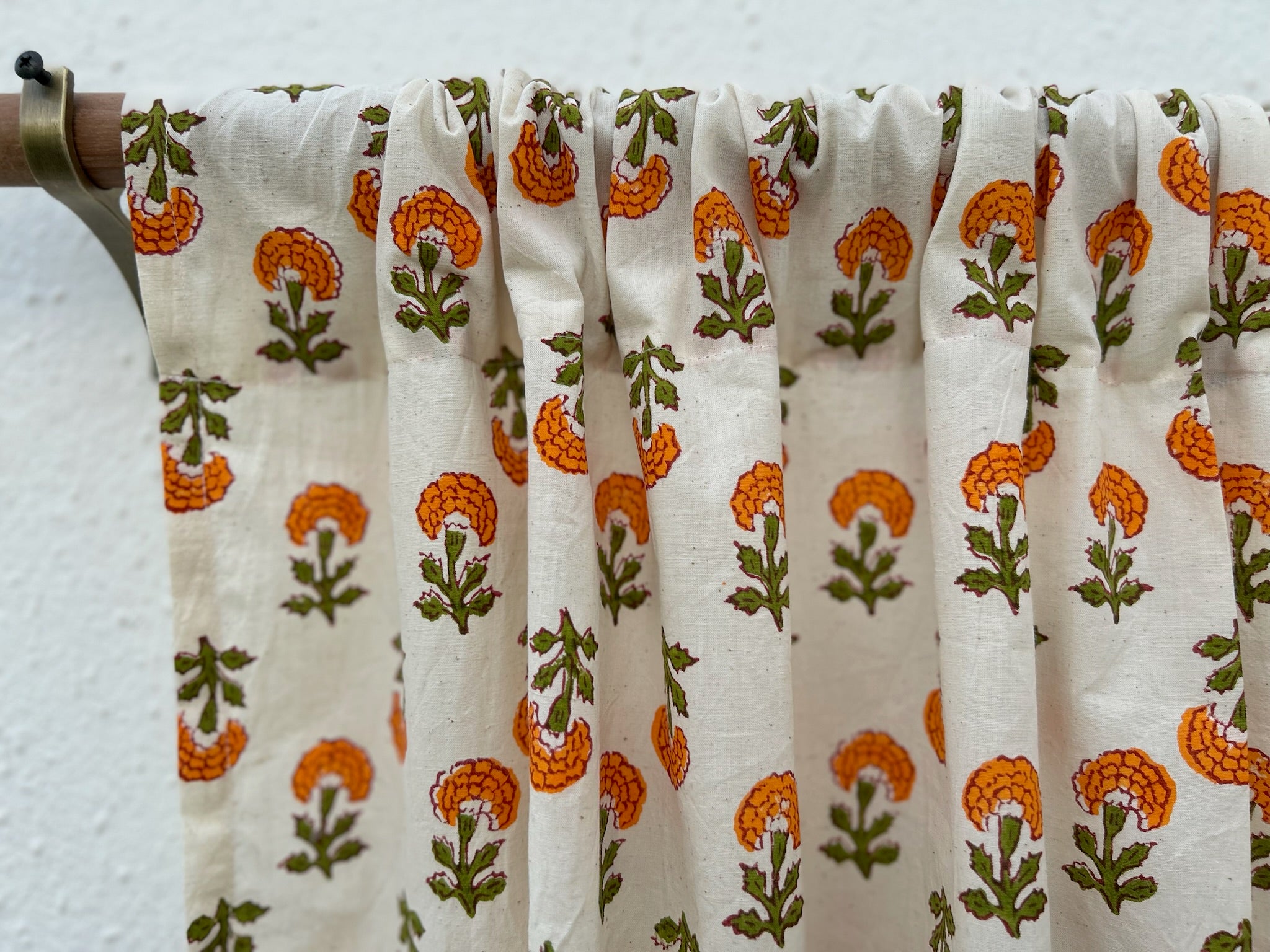 Fabric with orange and green floral pattern draped over a wooden rod against a white background