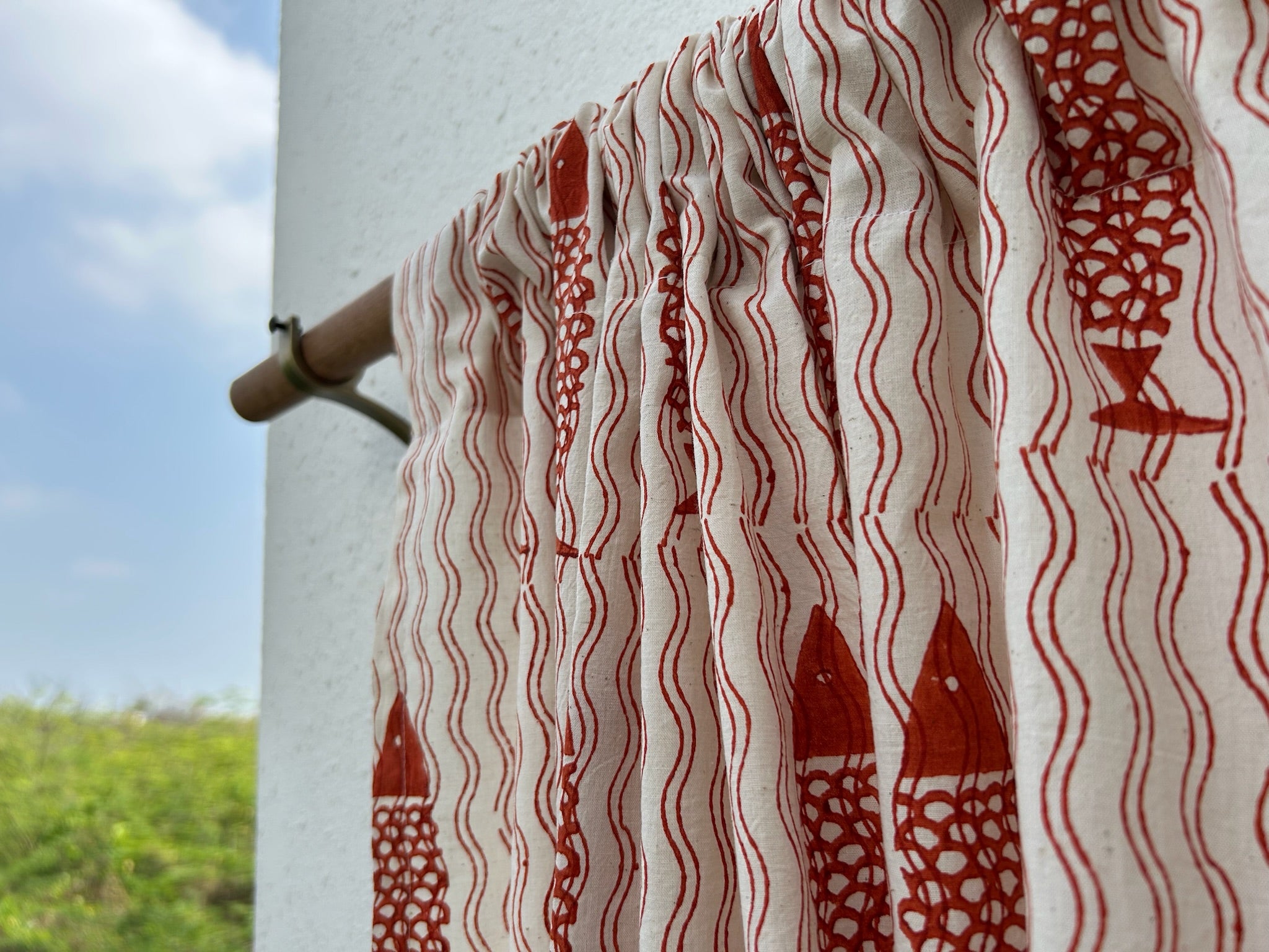 Red and white patterned fabric on a clothesline with a blue sky and greenery in the background