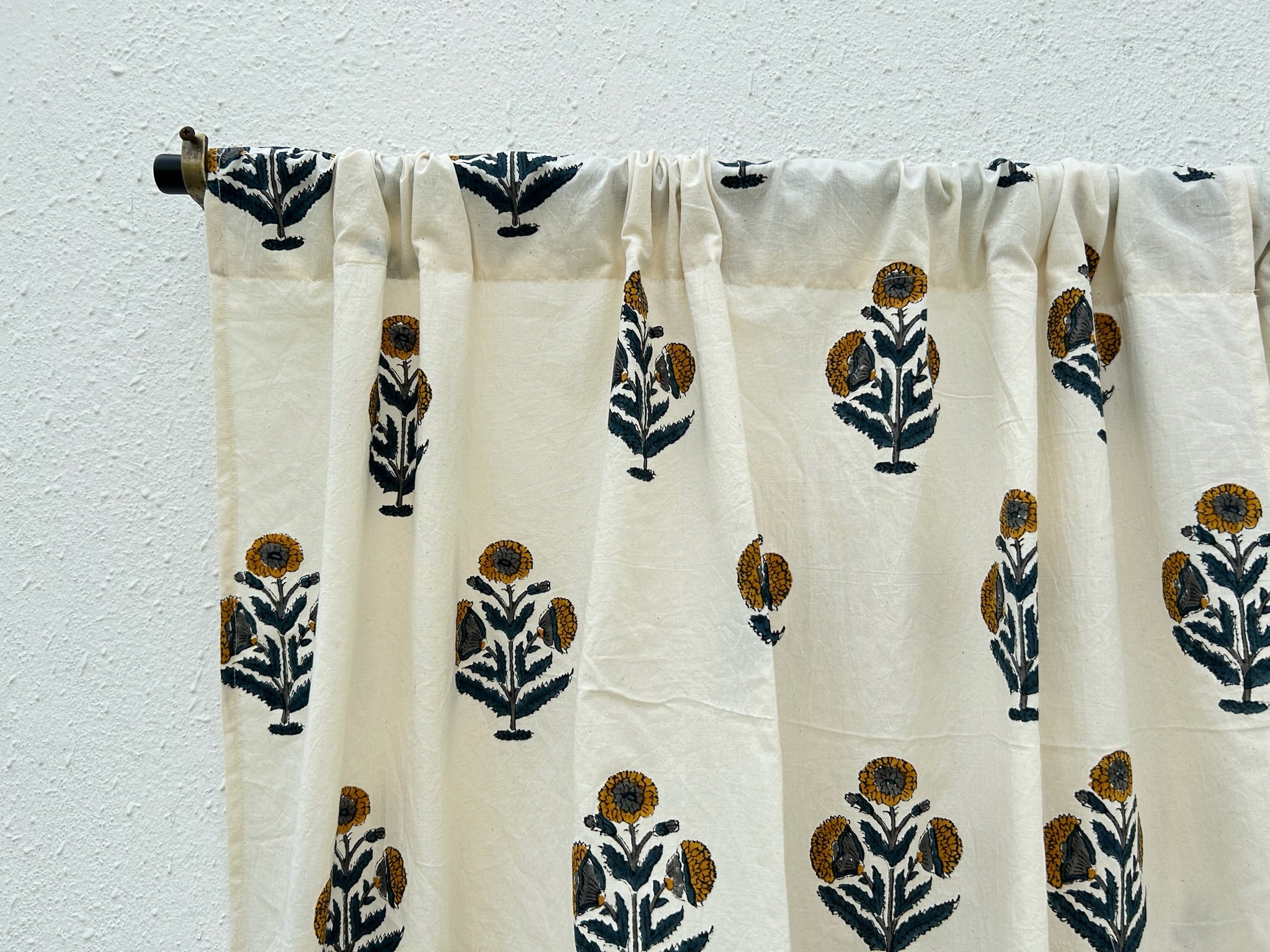 White curtain with black and brown floral patterns hanging against a white wall.