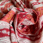 A close-up of draped fabric with a red and white block-printed floral and geometric pattern, featuring warm orange-yellow accents.