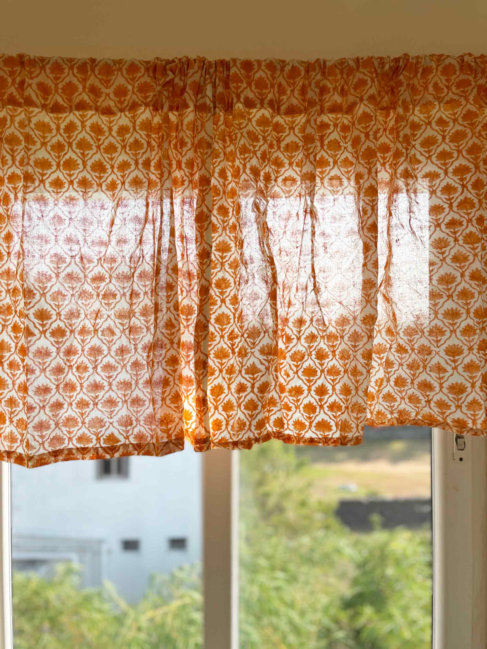 Orange patterned curtain with lace overlay in front of a window