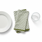 Stack of green patterned napkins on a white surface with a plate and glass.