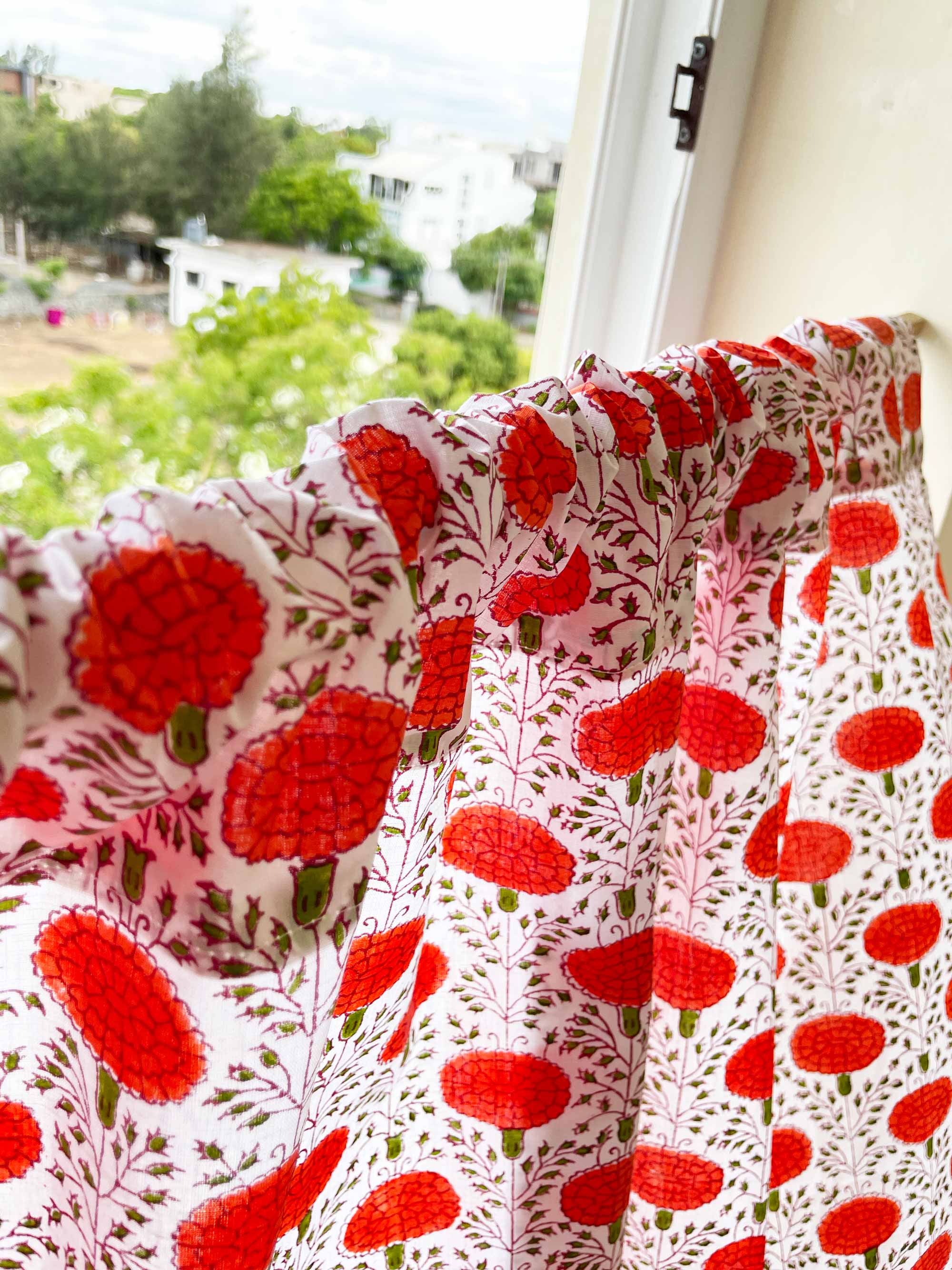 Floral patterned fabric with red flowers on a white background, hanging by a window.