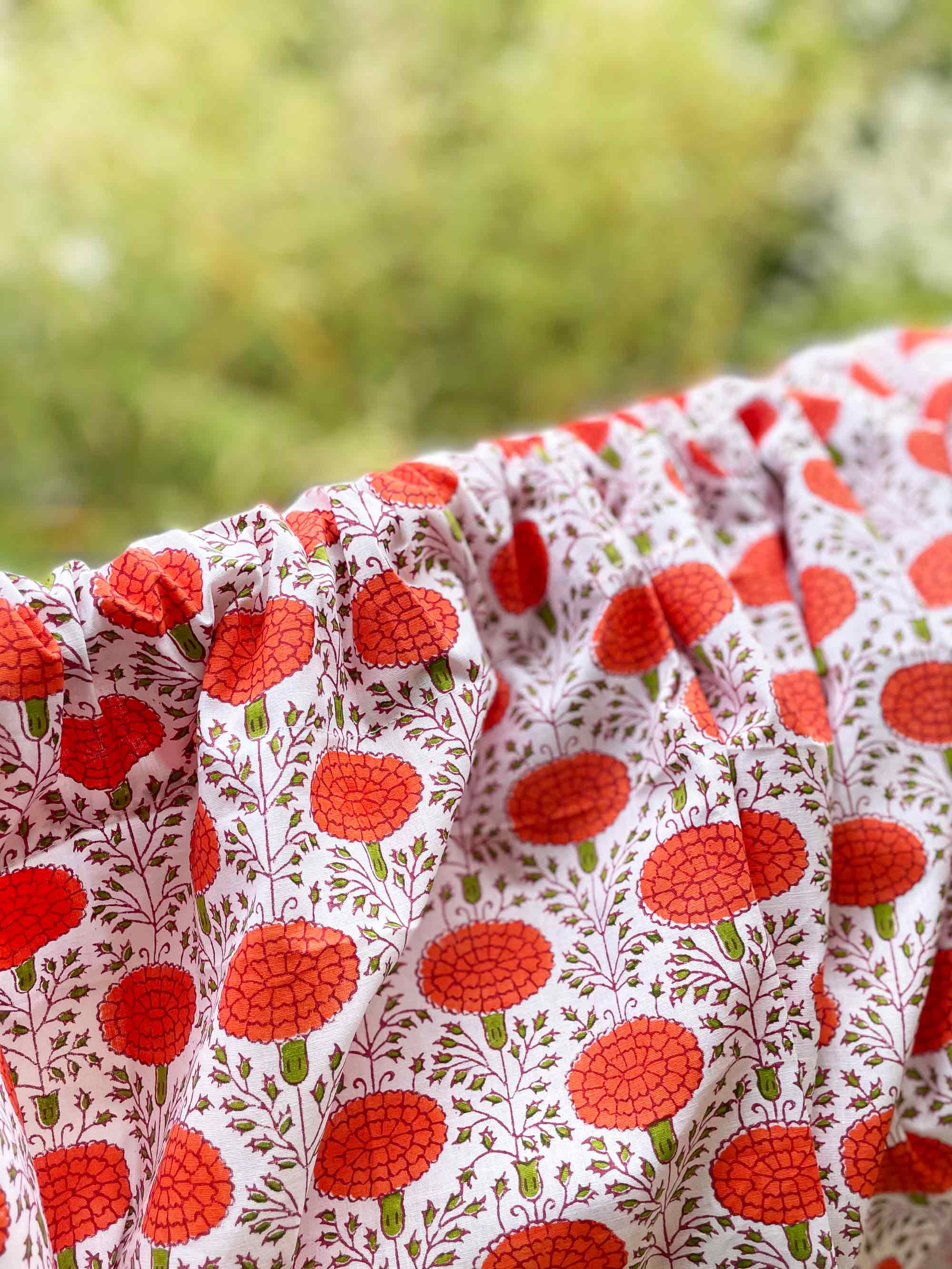 Close-up of fabric with red floral pattern against a blurred natural background