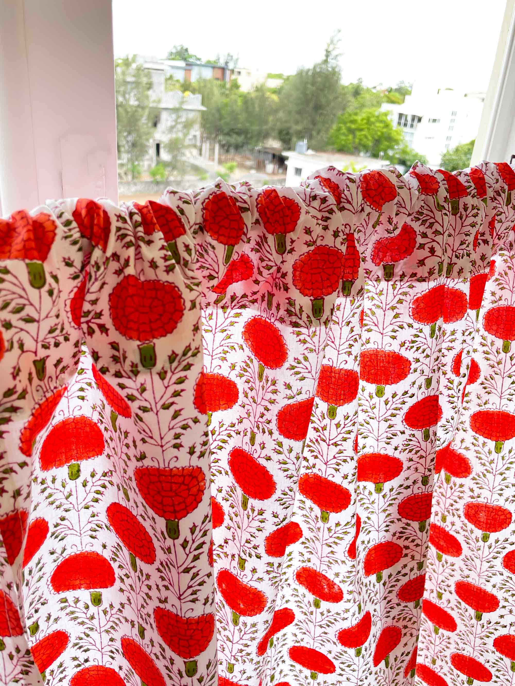 Red floral patterned fabric draped over a window with a view of greenery outside.