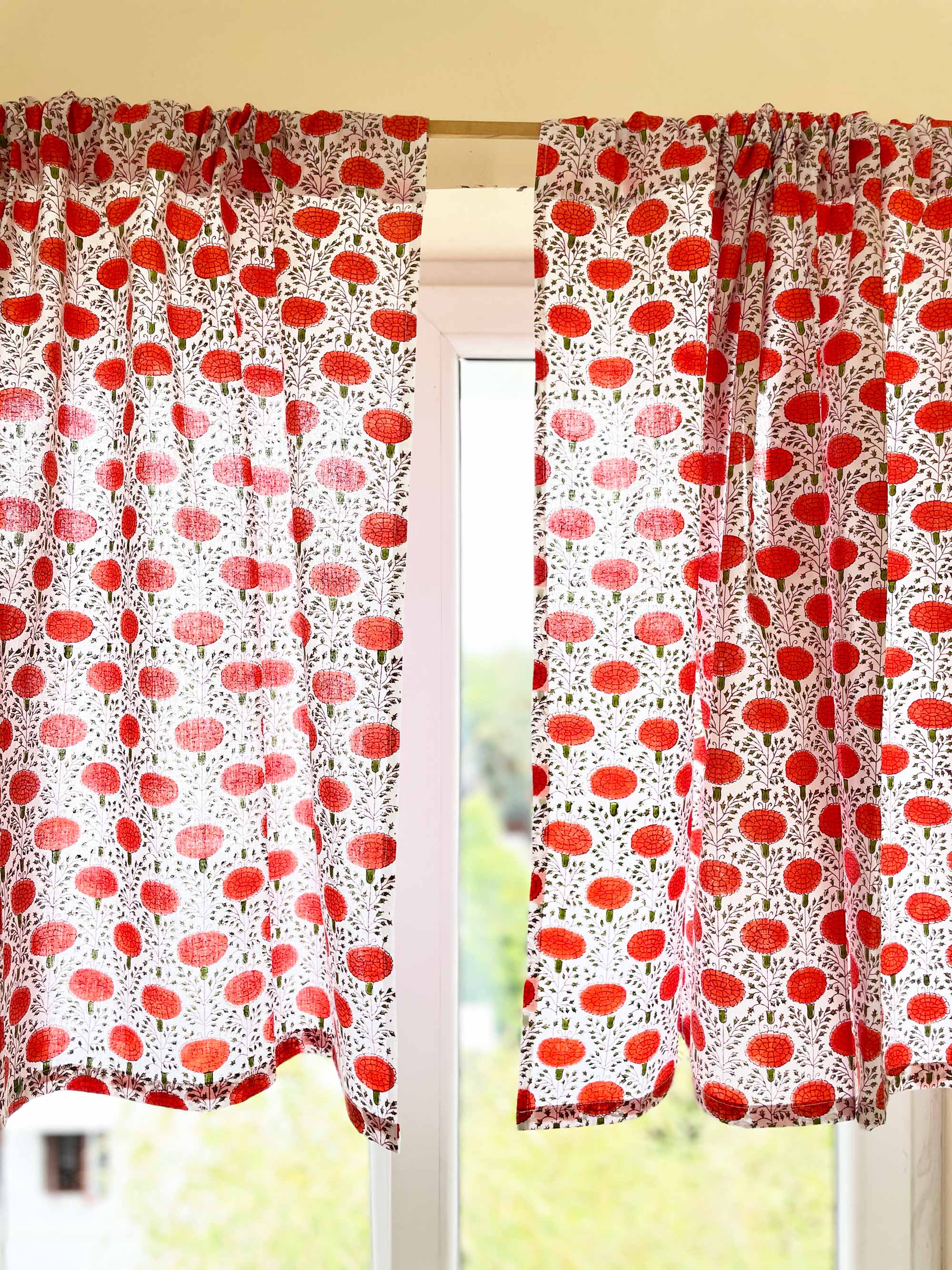 Red and white patterned curtains on a window with blurred greenery in the background.