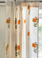 Sheer curtain with floral embroidery in orange and green on a white background