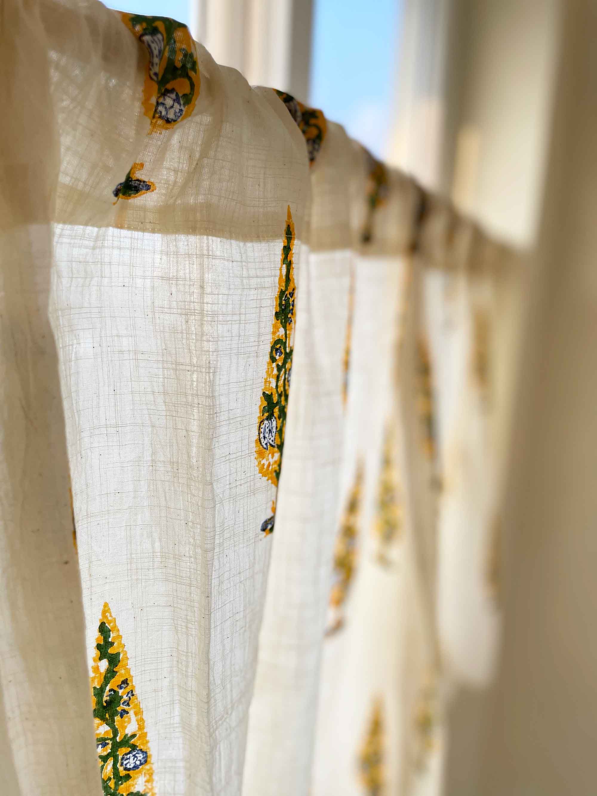White fabric with yellow floral patterns hanging against a bright background